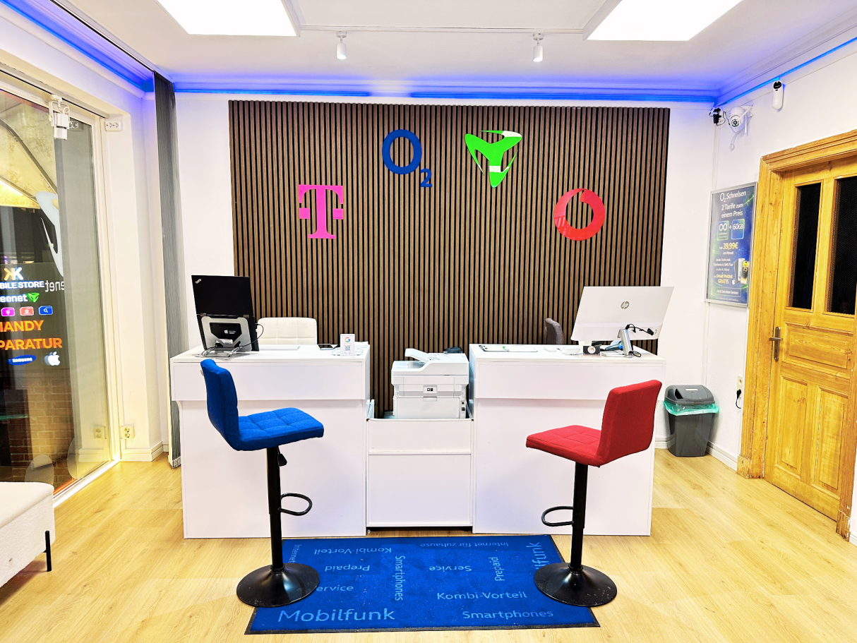 Moderner Mobilfunkshop mit zwei Barhockern in Rot und Blau, Markenlogos von O2 Telekom Freenet & Vodafone an der Wand.
